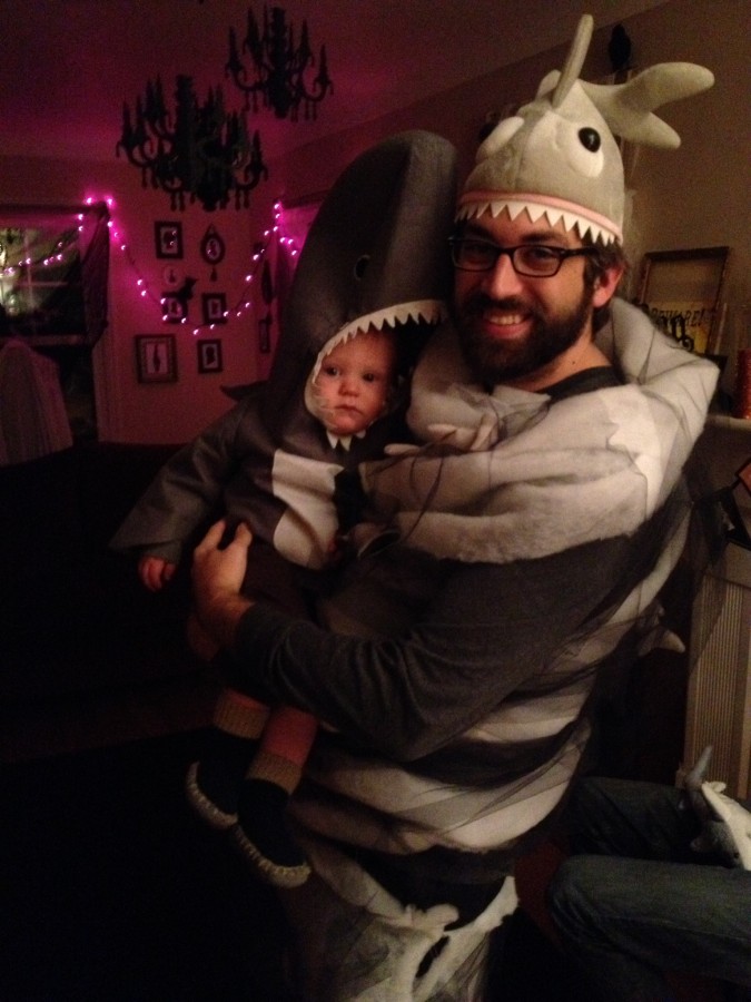 Man dressed as Sharknado holding a small child dressed as a shark.